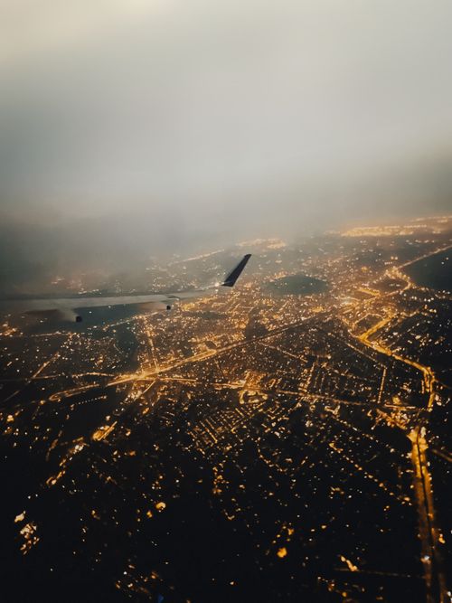 Free A dramatic aerial cityscape with glowing city lights viewed from an airplane during night flight. Stock Photo