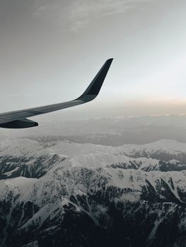 A breathtaking aerial view of snow-covered mountains with an airplane wing in sight.