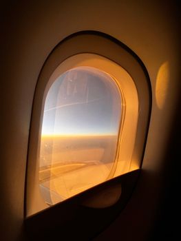 Warm sunset view through an airplane window, capturing a serene sky and wing at high altitude.