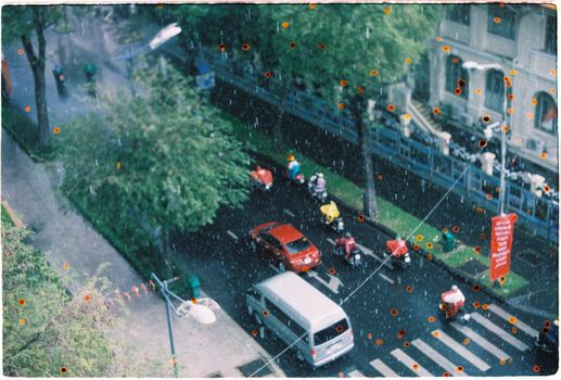 Vivid urban street captured from above with vehicles moving in the rain.