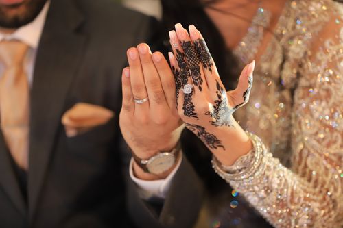 Free Close-up of a couple's hands displaying rings and intricate henna in a wedding setting. Stock Photo