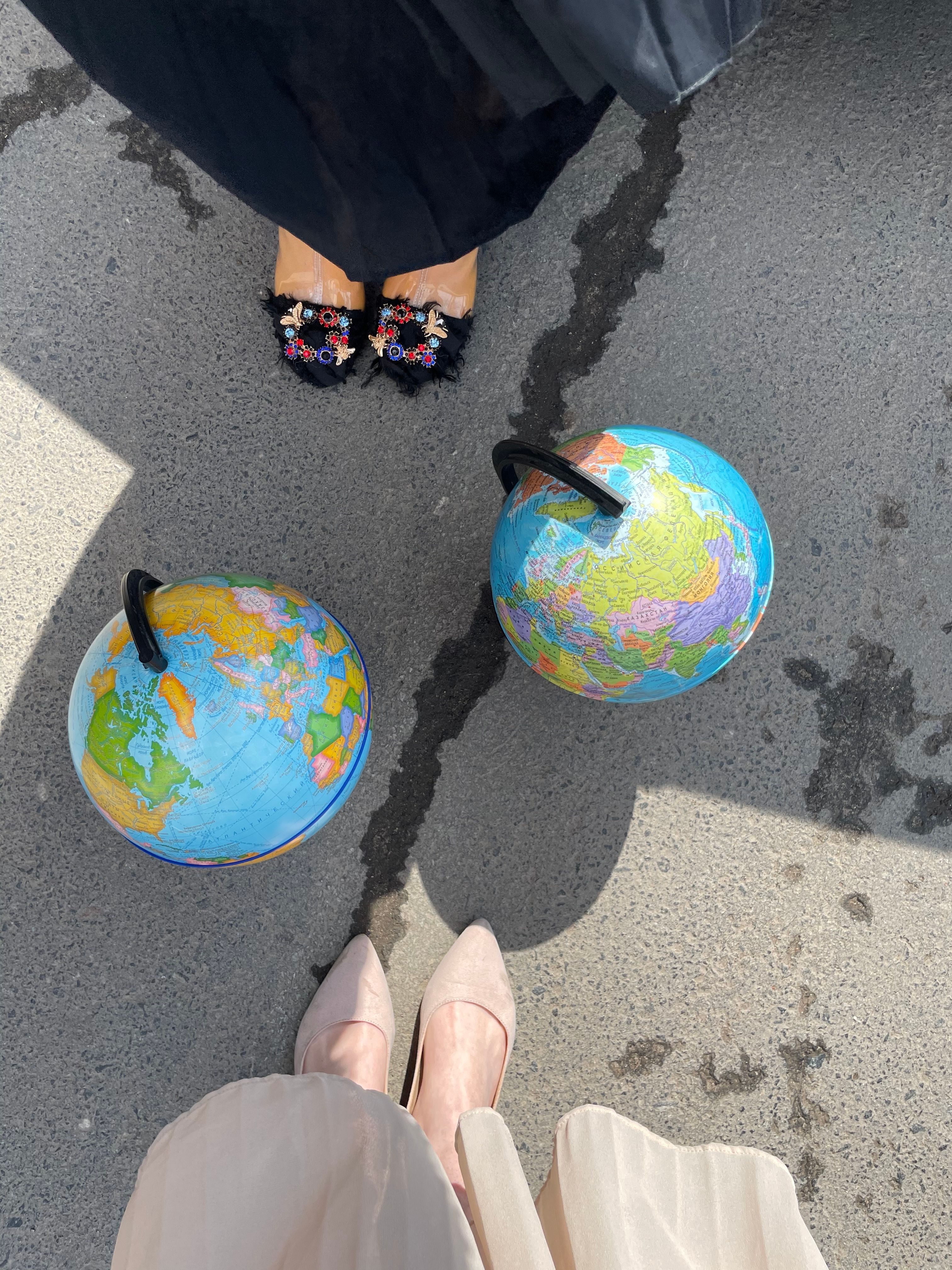 High angle view of two colorful globes on pavement with women's stylish shoes in frame.