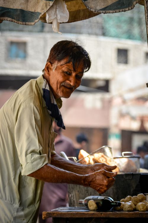 Free Elderly vendor preparing food at a bustling street market in Karachi, showcasing local culture. Stock Photo
