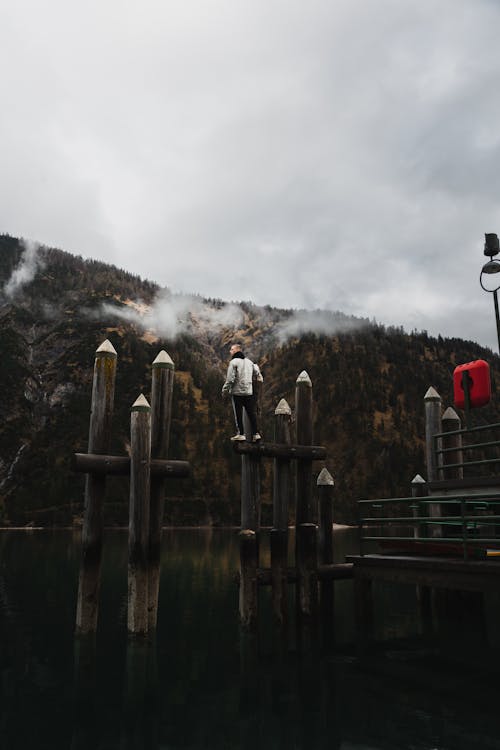 A Man Standing on Wooden Post on Water