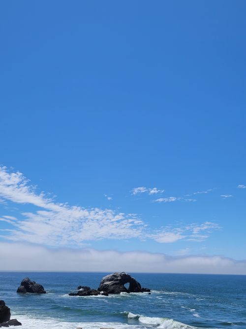 Free Peaceful seascape featuring ocean waves, rocky formations, and a bright blue sky. Stock Photo