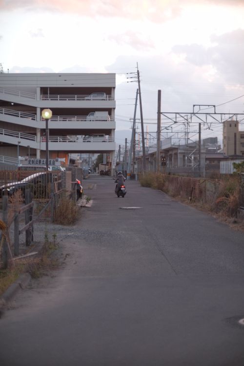 Free A person riding a scooter on an urban street at sunset with nearby buildings and infrastructure. Stock Photo