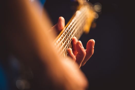 Detailed shot of fingers playing an electric guitar with a blurred background.