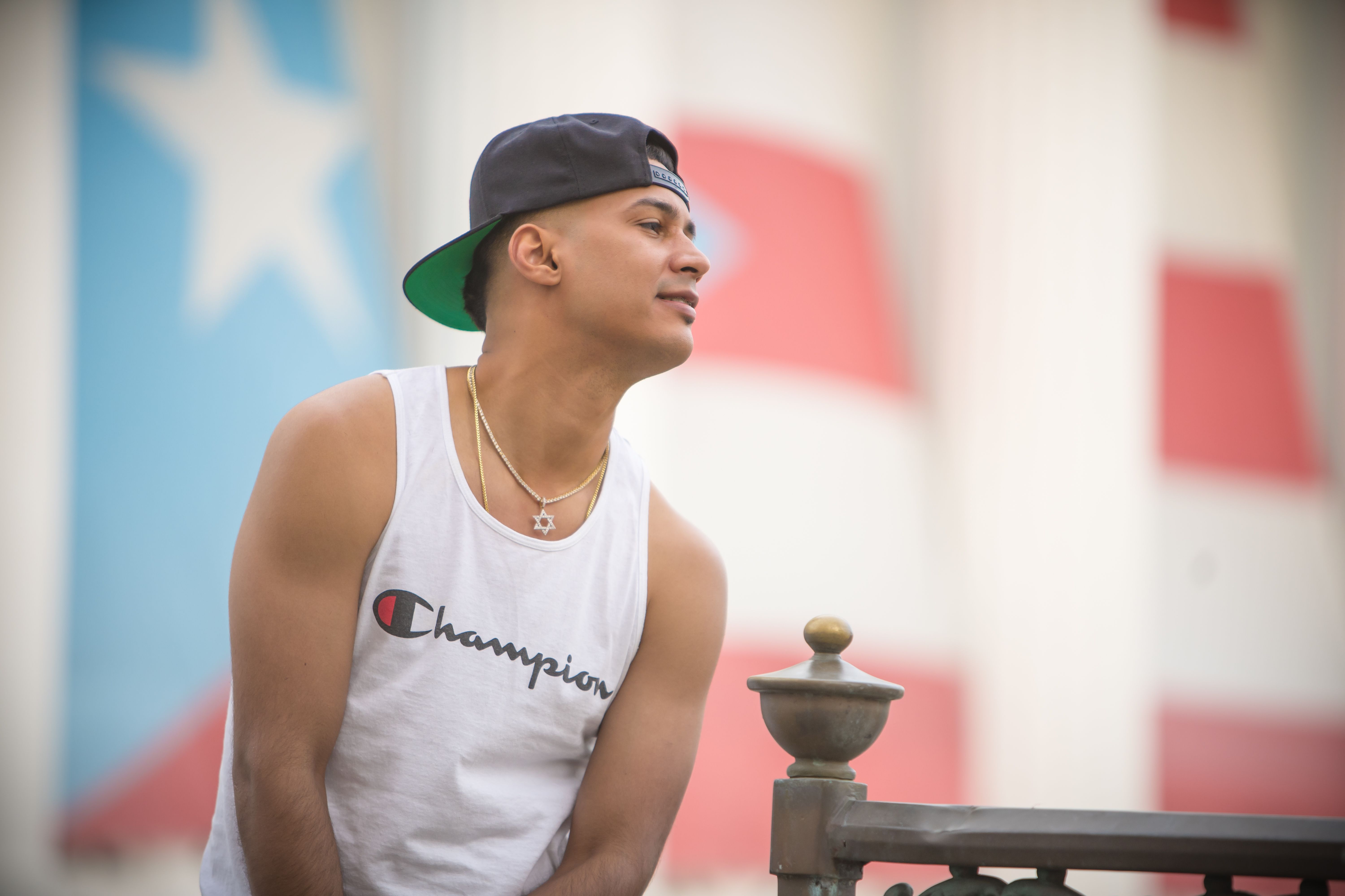 Stylish young man in a sleeveless shirt leaning on a railing outdoors.