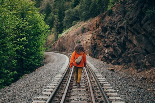 Woman in Orange Jacket Walking on the Railroad