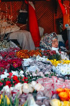 A vibrant flower stall with various blooms and a vendor wearing a headscarf.