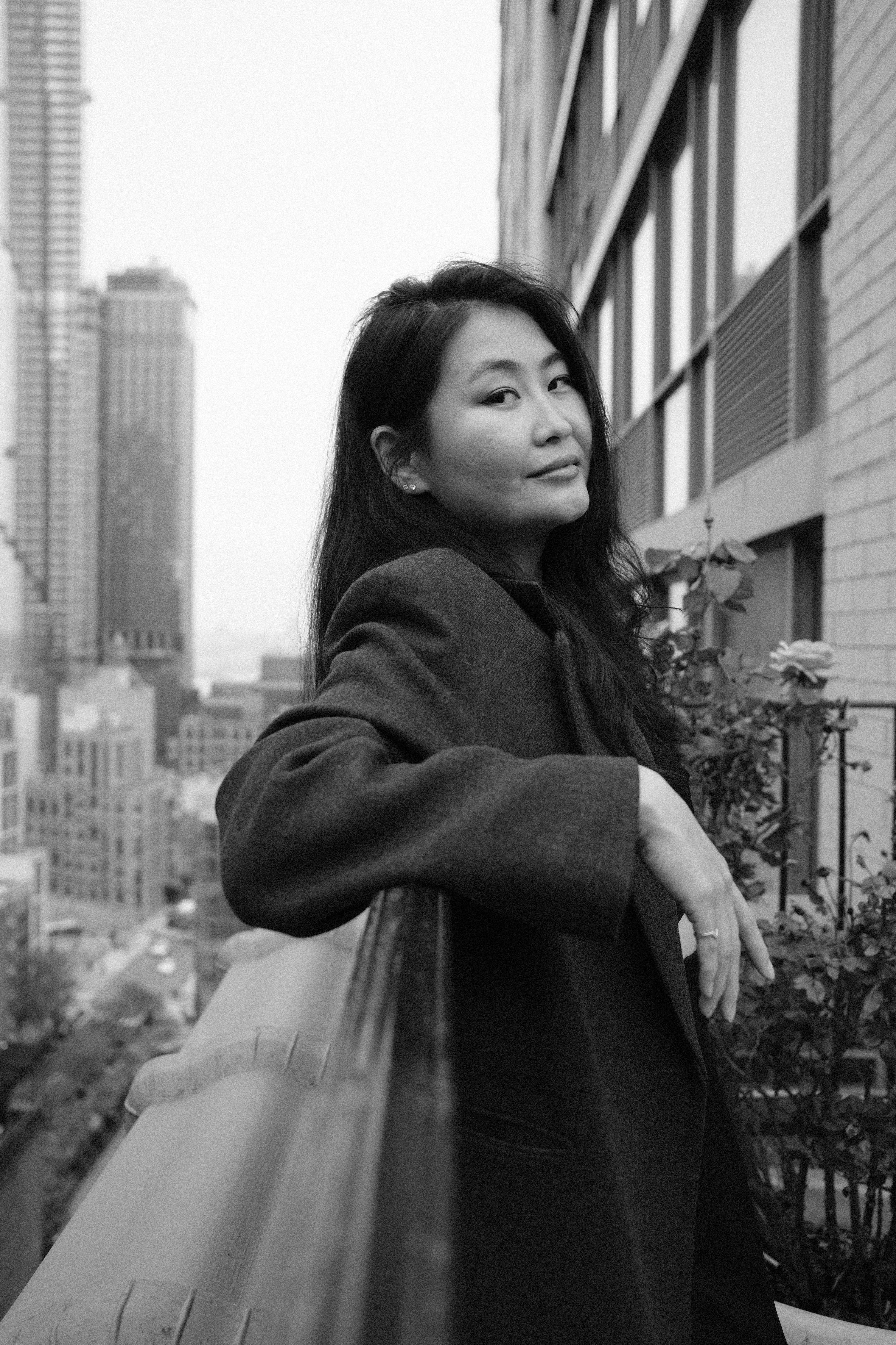 A stylish black and white portrait of a woman posing on a balcony overlooking the cityscape.