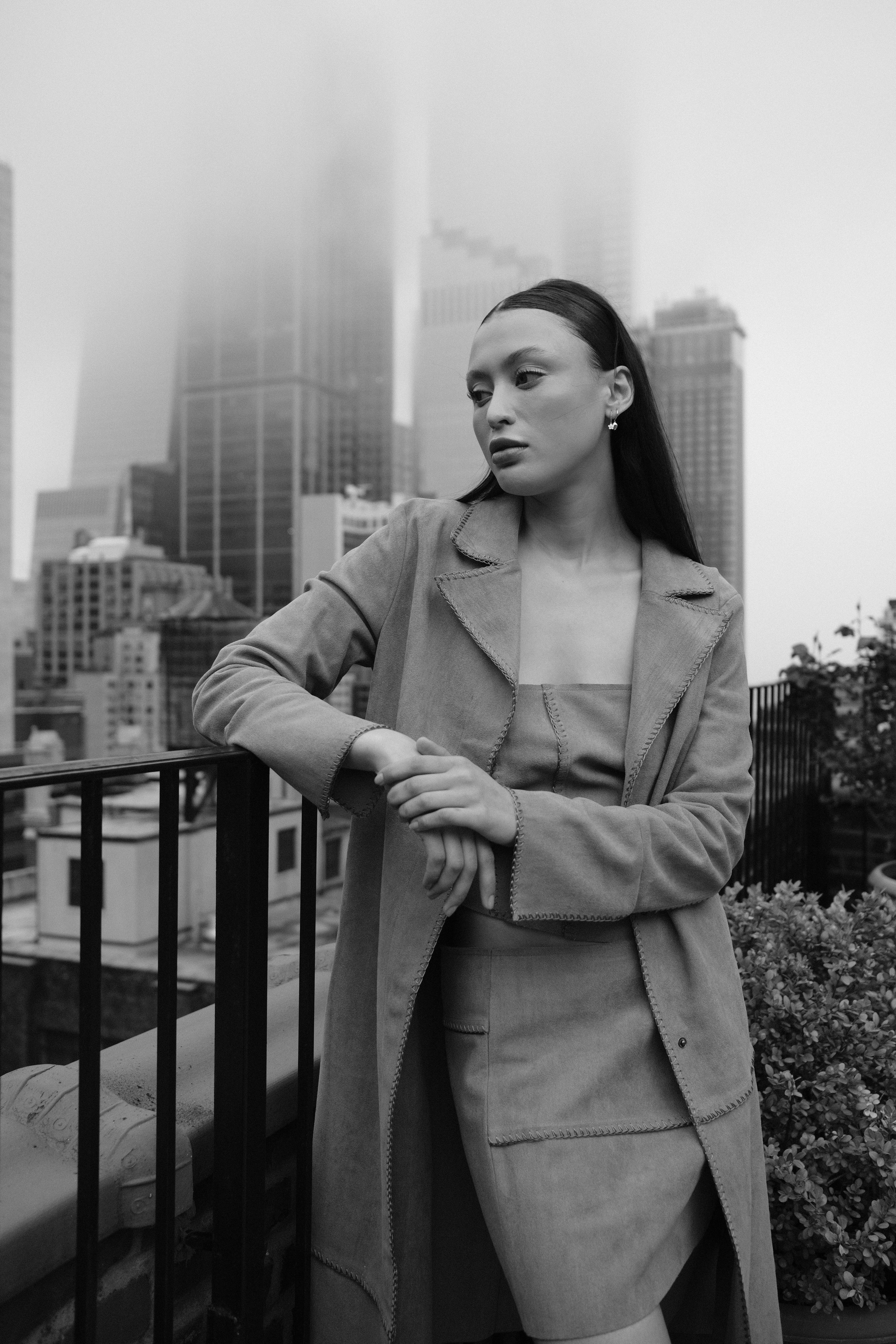 Stylish woman in modern fashion posed on a foggy balcony with city skyscrapers.