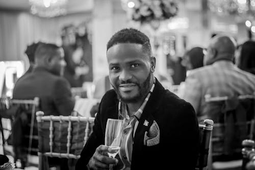 A Grayscale Photo of a Man in Black Suit Holding a Champagne Glass