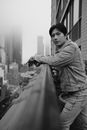 Grayscale Photo of Woman in Jacket and Pants Standing on Top of Building