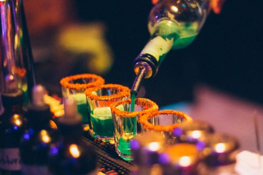Colorful cocktails being poured into glasses with orange rims at a lively bar setting, perfect for parties.