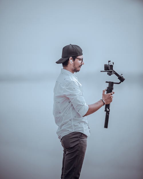 A Side View of a Man in White Long Sleeves Holding a Tripod with Camera