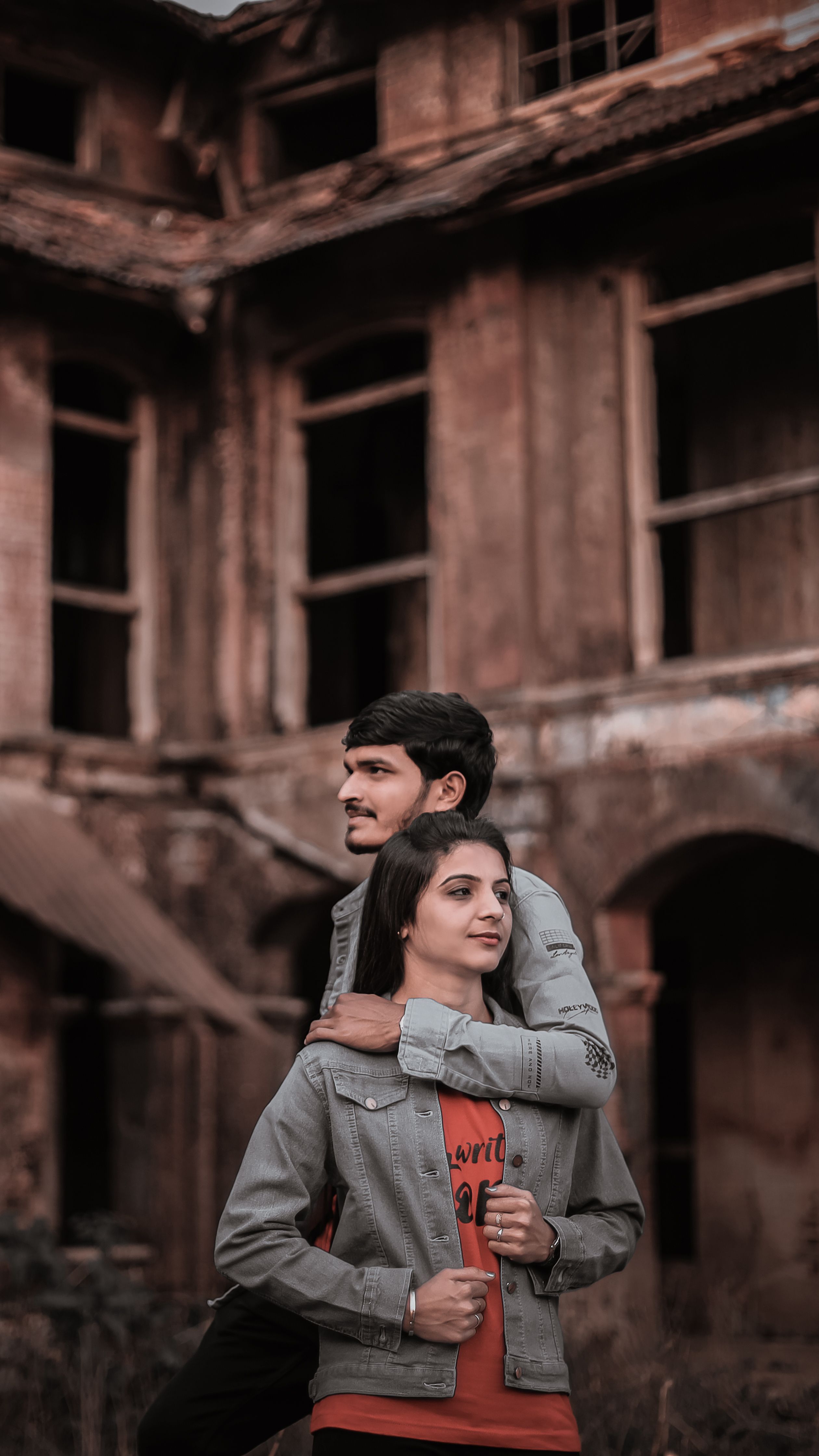 A young couple embraces in front of a rustic, weathered building, exuding warmth and affection.