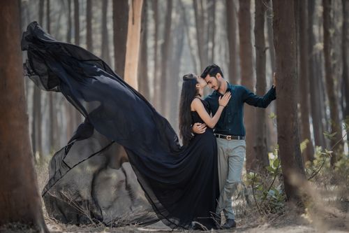 Free A romantic couple embraces in a forest, showing affection and love. Nature setting with flowing black attire. Stock Photo