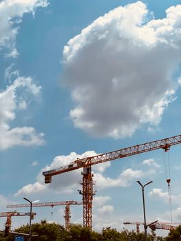 Cranes working at a construction site under a vibrant blue sky and fluffy clouds.