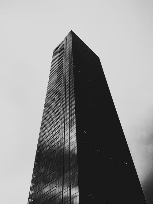 Free Dramatic black and white view of a towering skyscraper against a cloudy sky from below. Stock Photo