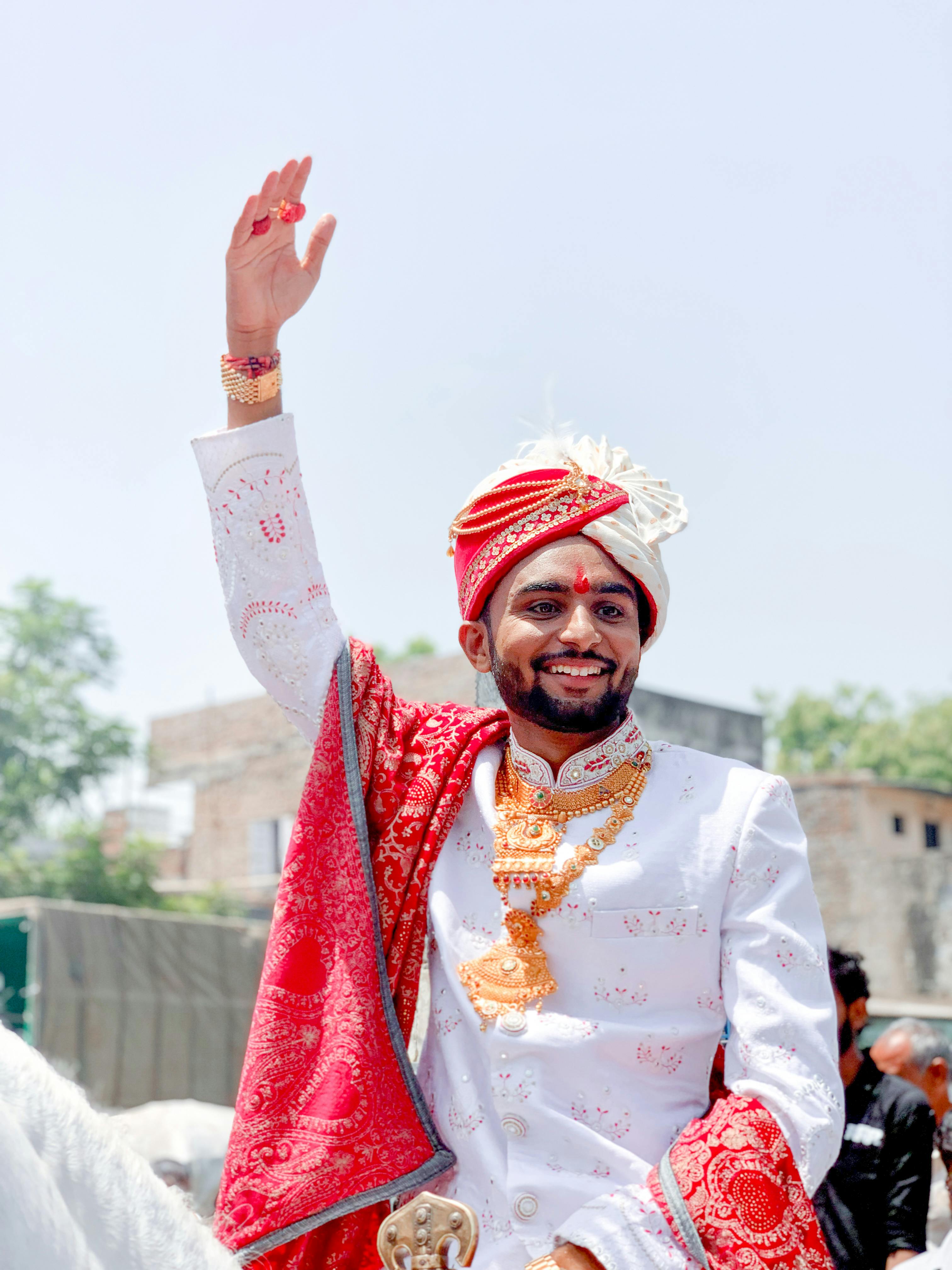 Smiling Indian groom in traditional attire waves during wedding procession in Ahmedabad.