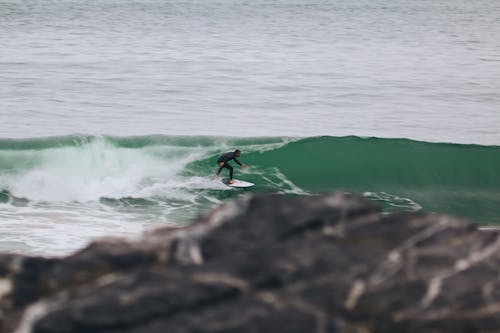 A Man in Black Wetsuit Surfing on the Beach