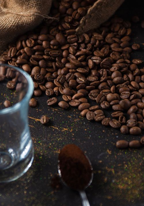 Free A pile of aromatic roasted coffee beans on a dark background with a clear glass and teaspoon. Stock Photo