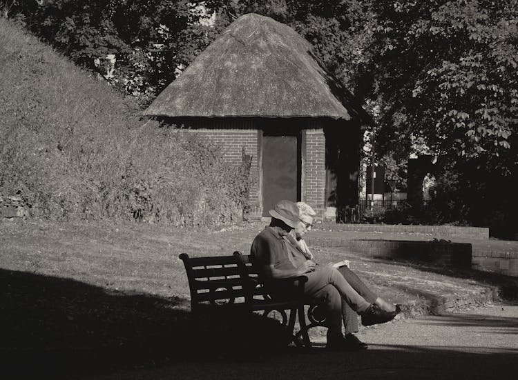 Grayscale Photo Of Two People Sitting On The Bench