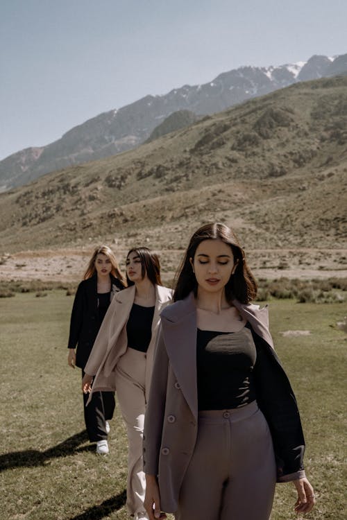 Fashionable Women Walking on Green Grass Field Near Mountains