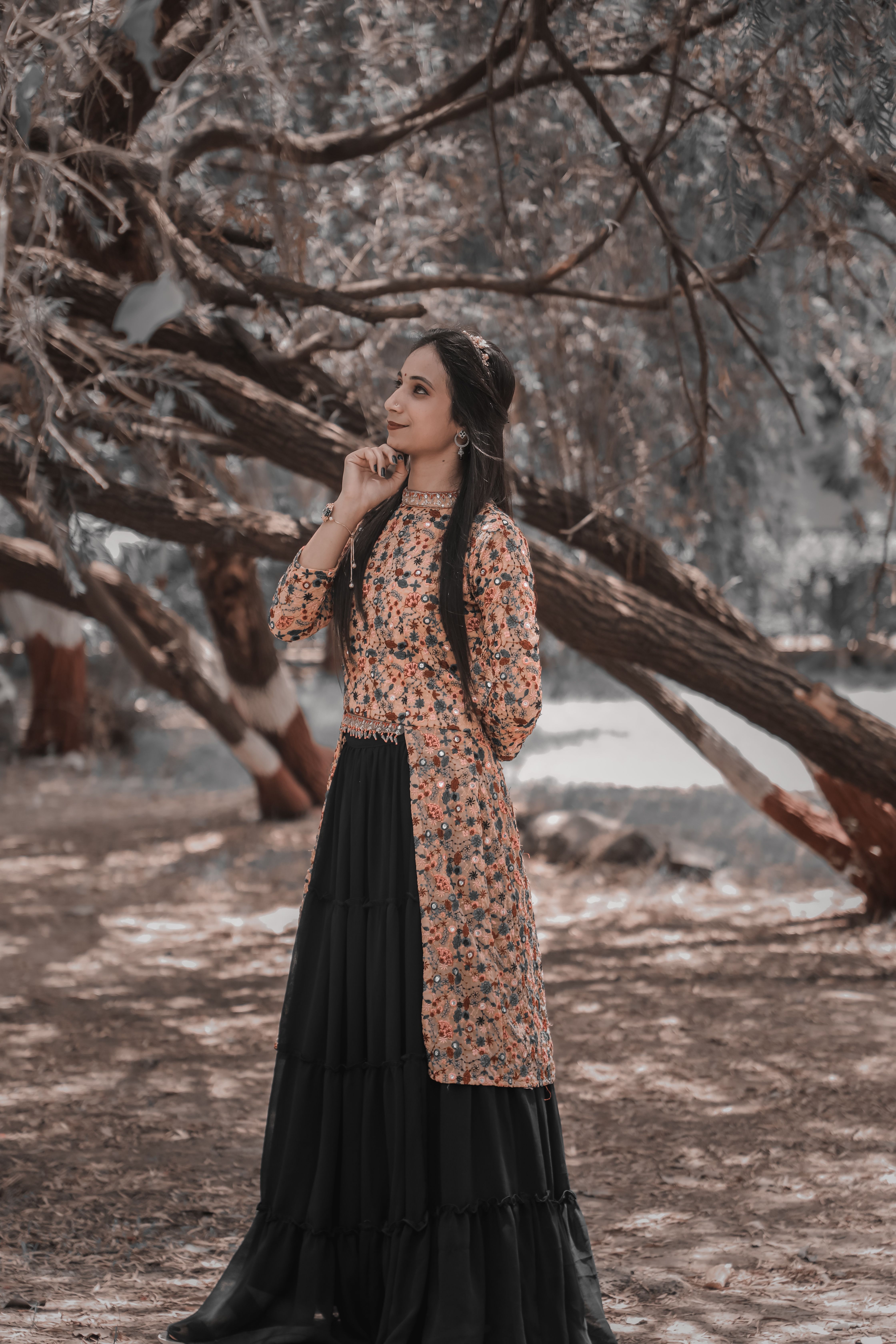Fashionable woman in floral top and black skirt posing thoughtfully under a tree outdoors.