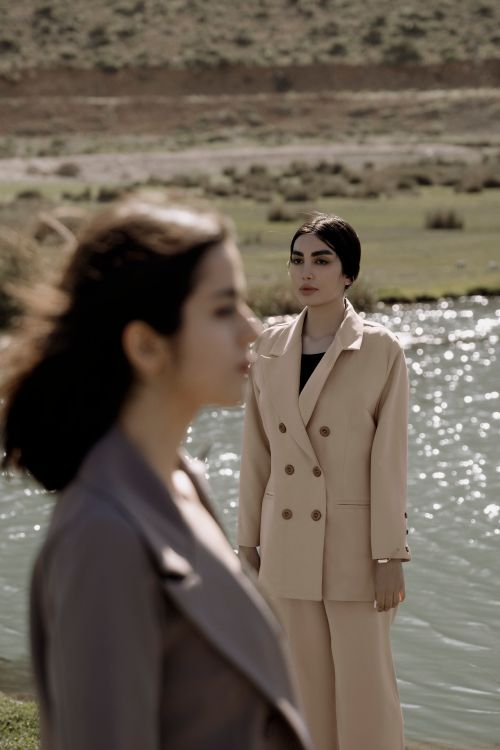 Free Two women in stylish suits stand by a tranquil lake, exuding elegance and poise. Stock Photo