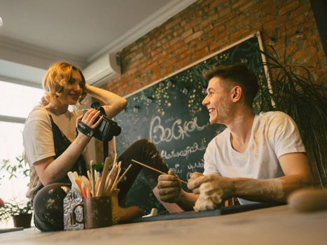 Smiling young adults engage in clay crafting and filming in a cozy indoor setting.