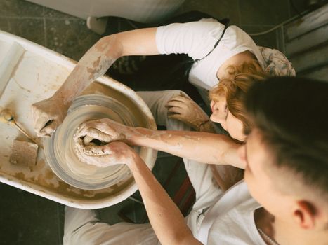 Couple enjoying pottery making together, engaged in handcrafting clay on a wheel indoors.