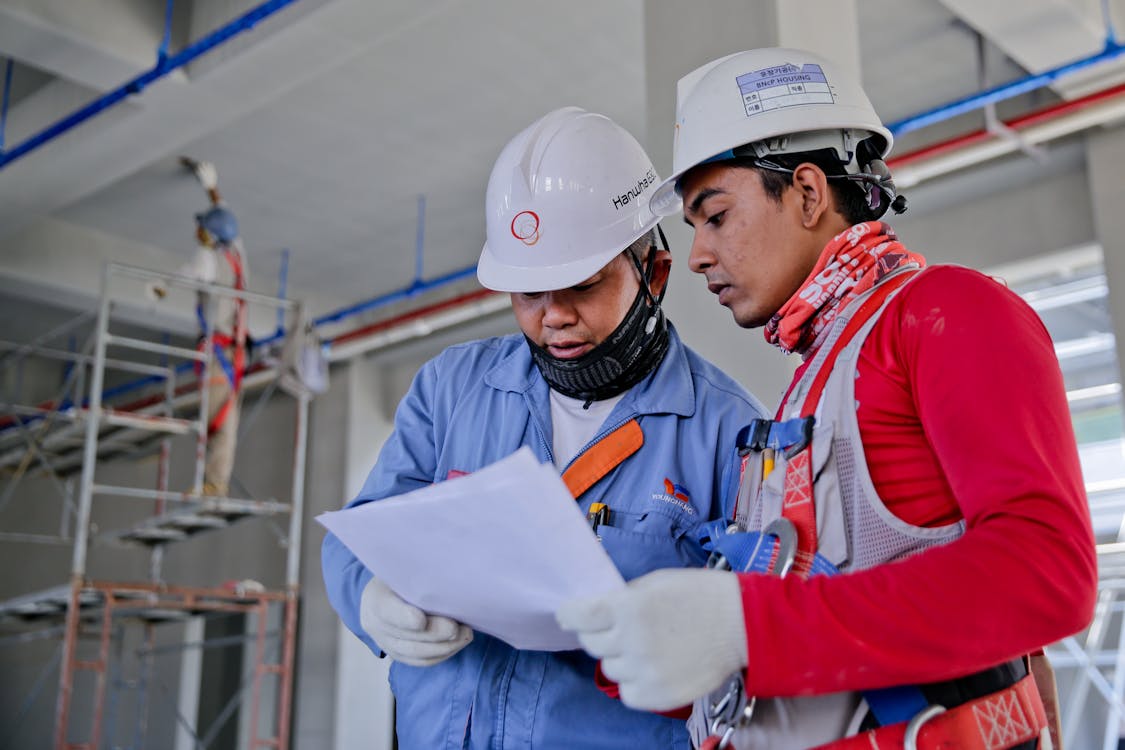 Two industrial workers discussing over documents at a site.