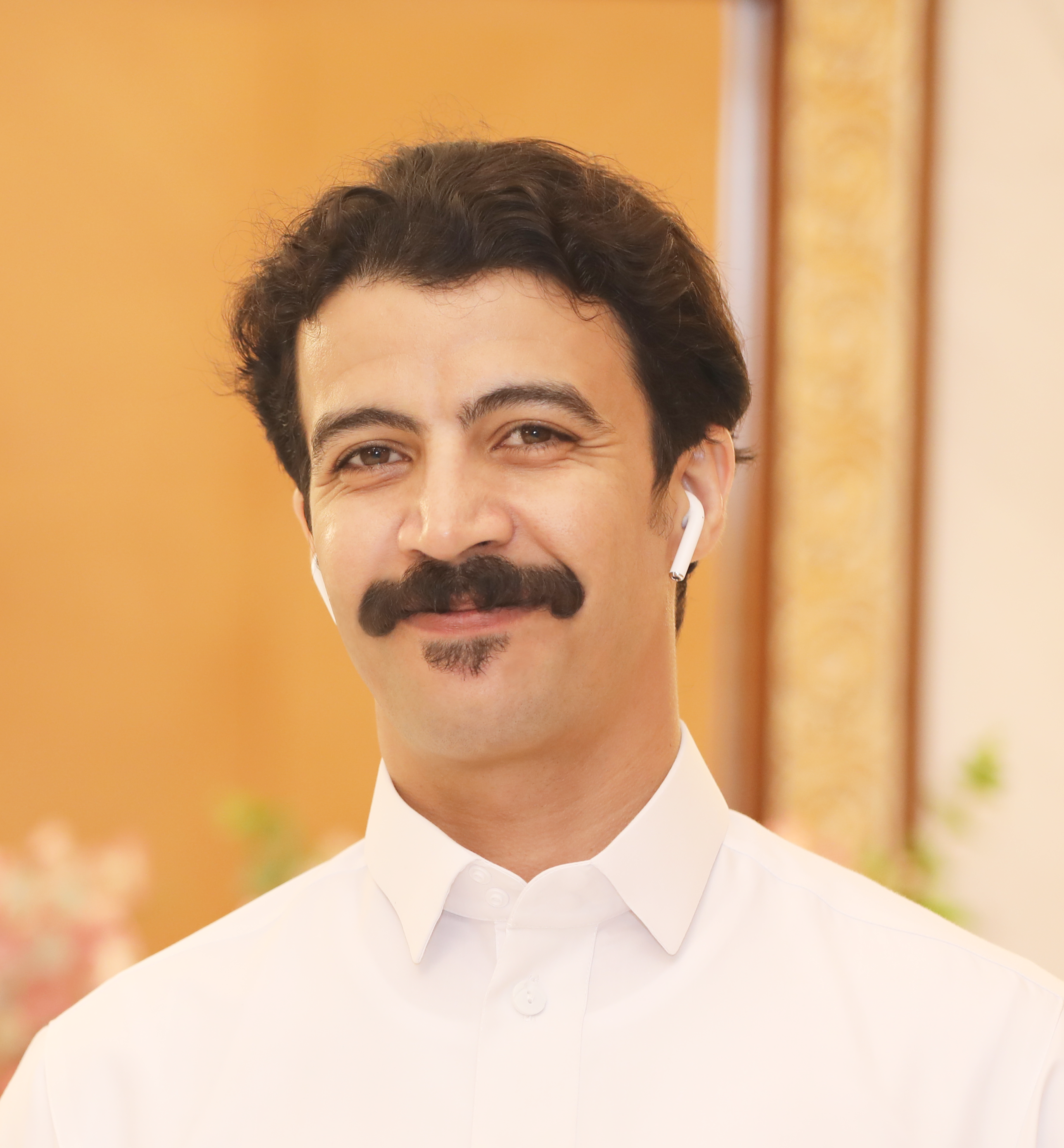 Portrait of a smiling man with a mustache wearing wireless earphones indoors.