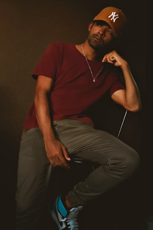 Free Man in Red Crew Neck T-shirt and Gray Pants Sitting on Chair Stock Photo