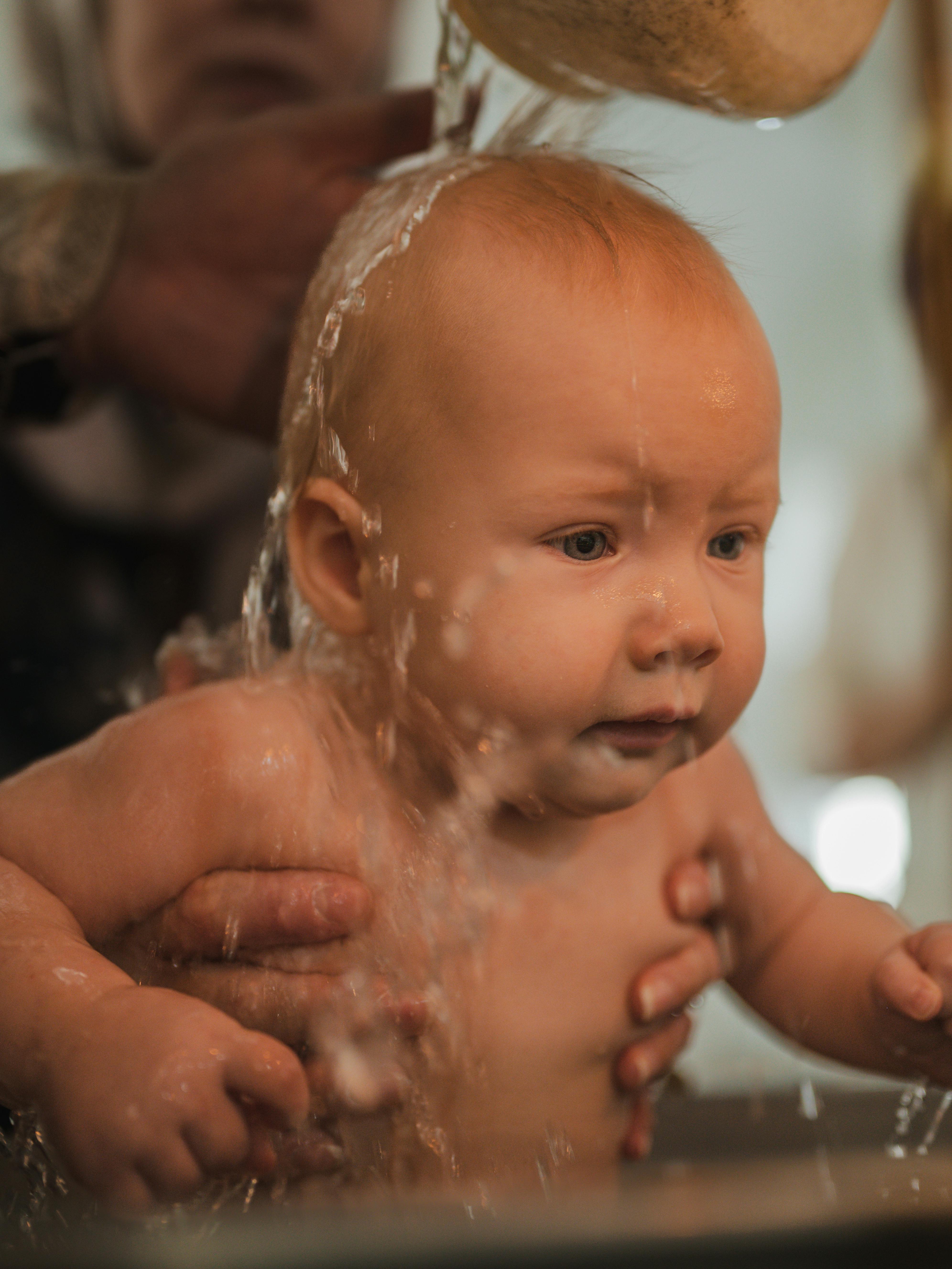 Emotional close-up of a baby experiencing baptism, capturing religious tradition and innocence.