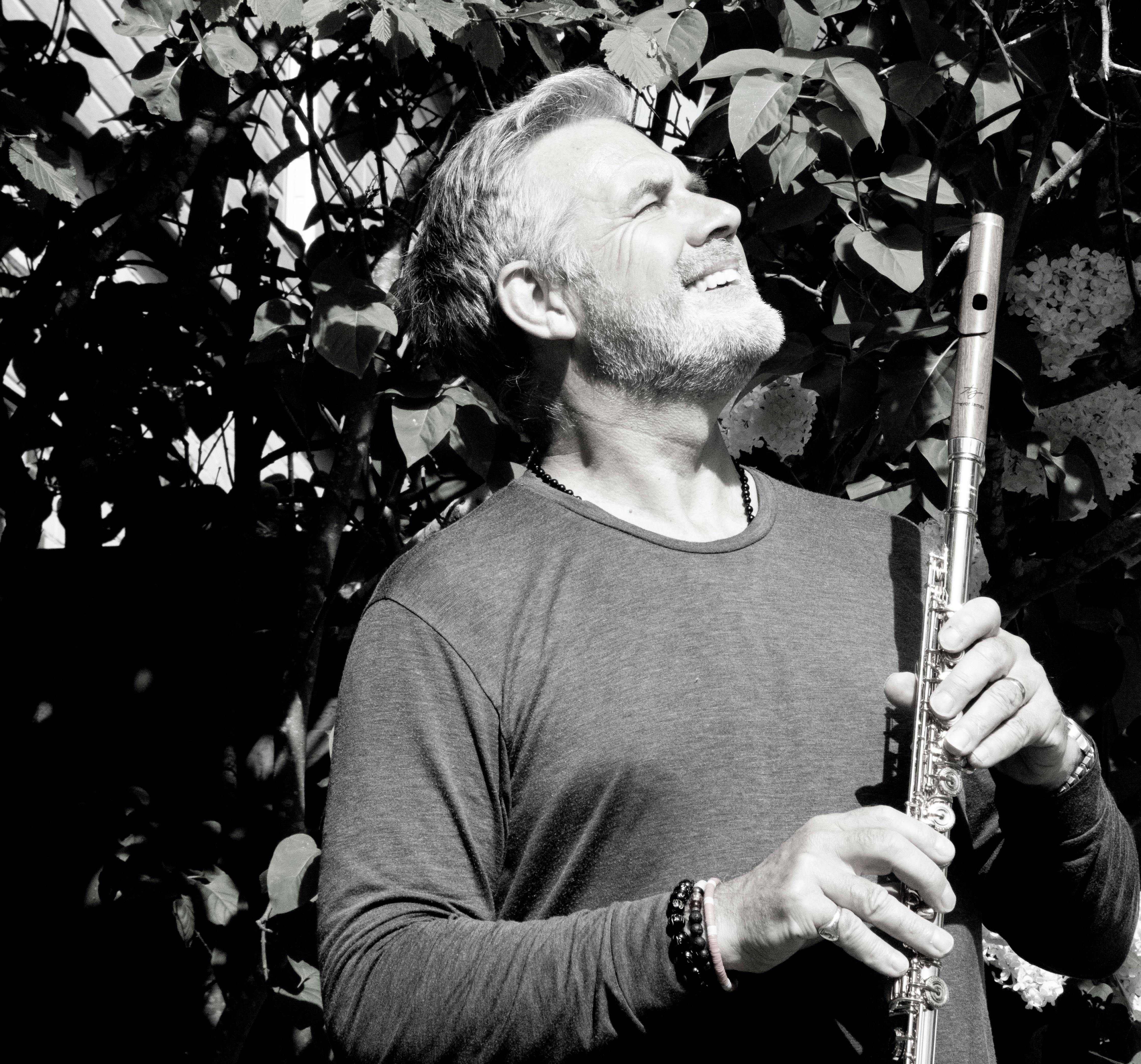 Black and white photo of a man playing flute outdoors in London, expressing joy and engagement with music.