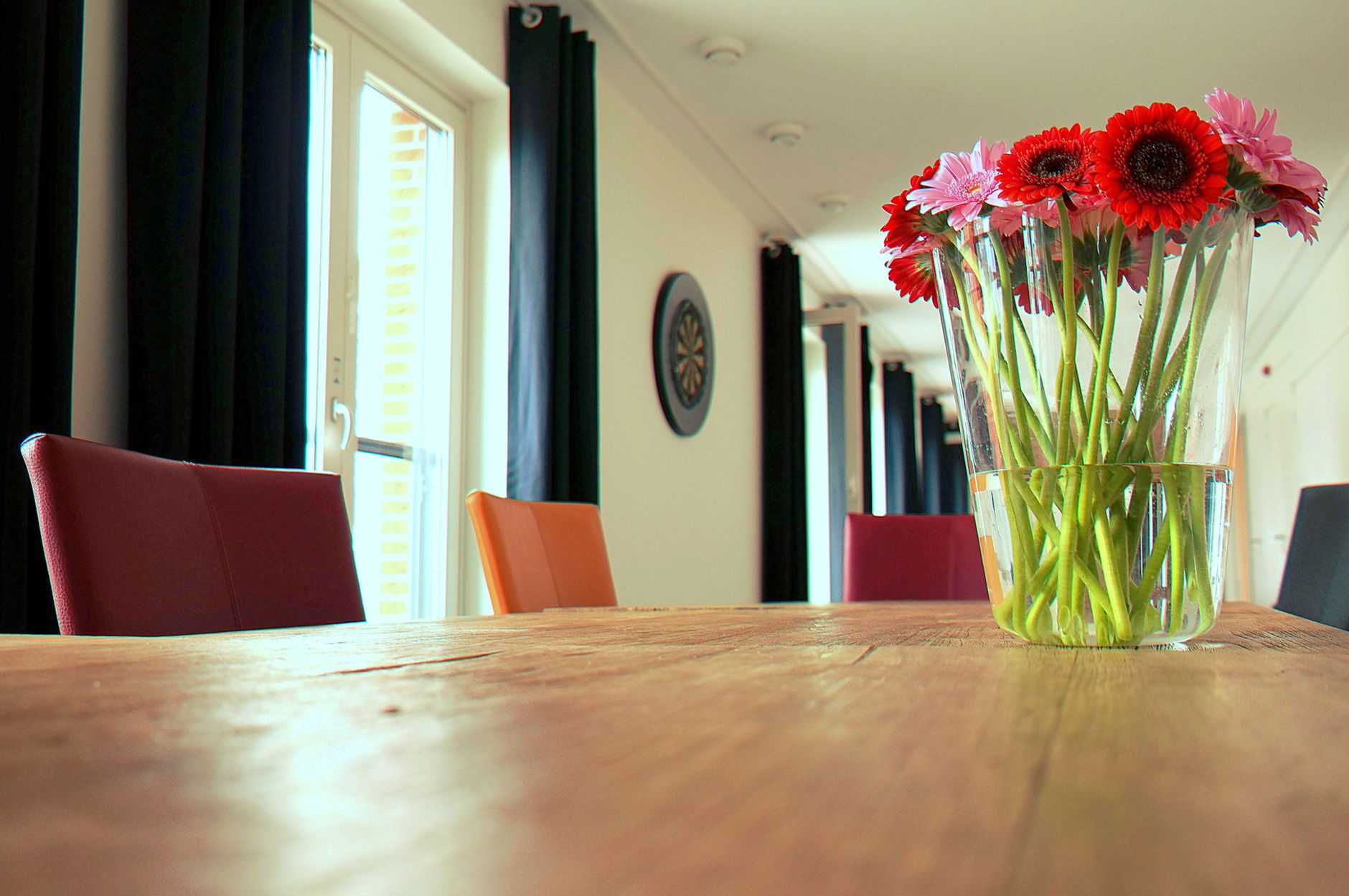 A contemporary dining room interior showcasing vibrant flowers in a vase on a wooden table.