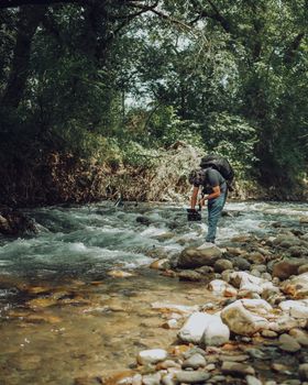 A videographer films a scenic river amidst lush green trees, showcasing nature's beauty.