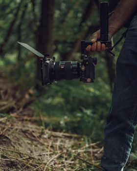 Professional cameraman holds camera with stabilizer in a lush forest setting.