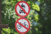 A pair of signs prohibiting motor vehicles and bicycles in a lush green area.