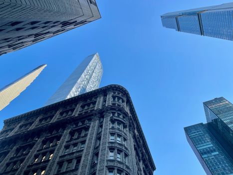 Low angle view of New York City skyscrapers against a clear blue sky, capturing urban architecture.