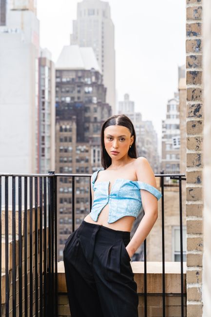 Stylish woman poses confidently on a city balcony with skyscrapers in the background.