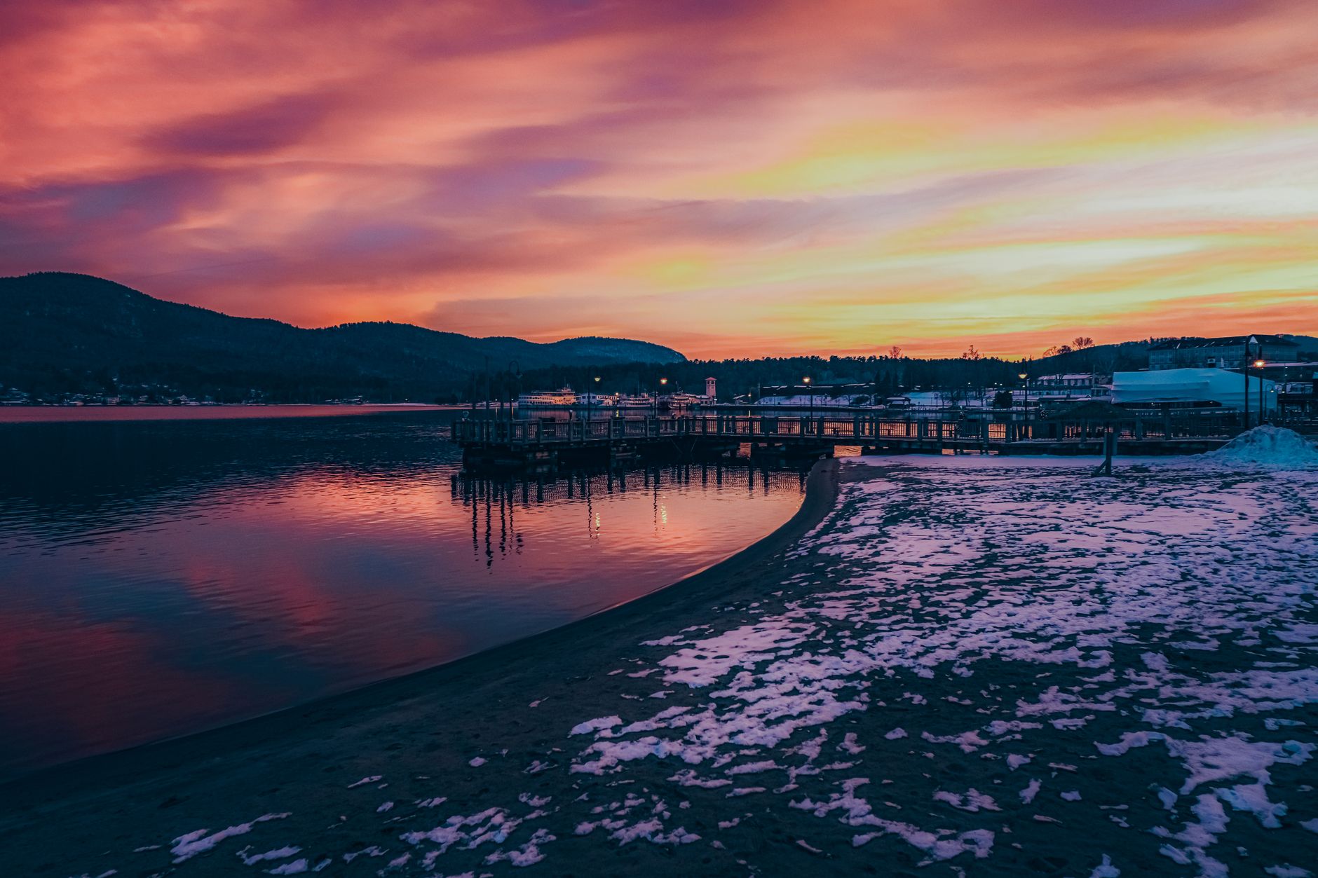 Breathtaking winter sunset over a serene lake with snow and a vibrant sky in the Adirondacks.