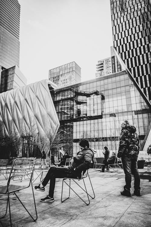 Grayscale Photo of Man Sitting on Chair Near Building