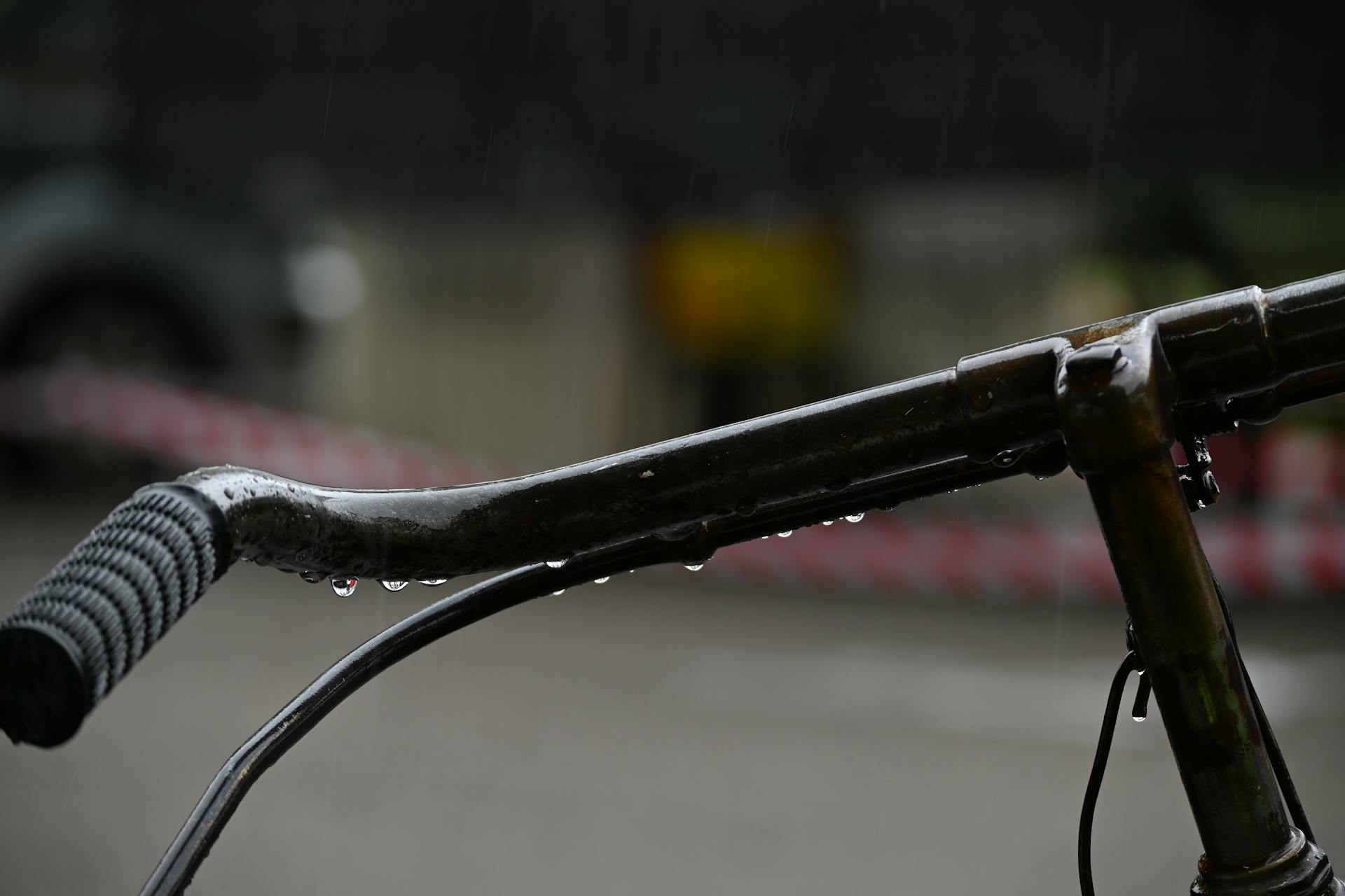 Detailed view of a bicycle handlebar with raindrops, highlighting transportation in rainy weather.