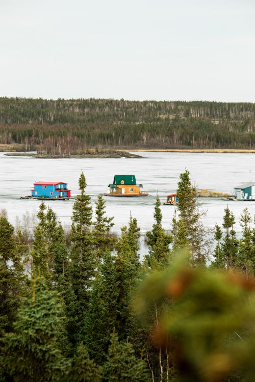 Free Floating houses on a frozen lake surrounded by snow-covered trees and forest in winter. Stock Photo