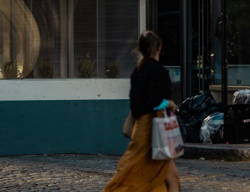Free A woman walking on a city sidewalk carrying shopping bags, passing a storefront window. Stock Photo