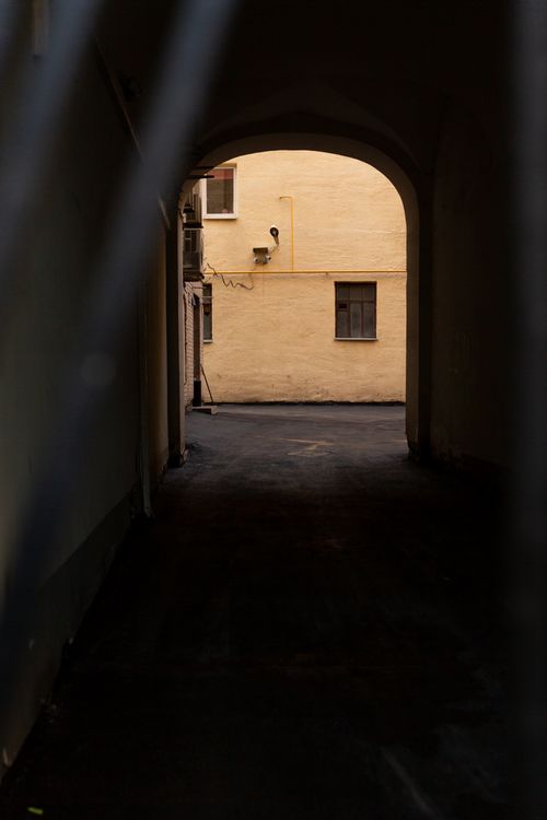 Free A shadowy view through a moody archway revealing a sunlit urban wall. Stock Photo